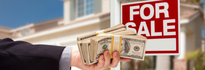 business man passing stack of hundred dollar bills in front of for sale sign