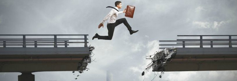 Man with briefcase jumping across broken bridge