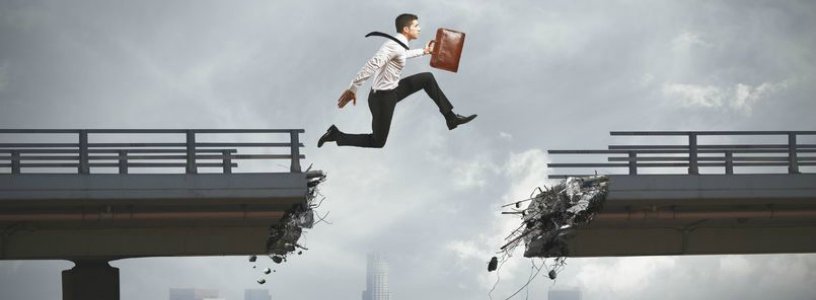 Man with briefcase jumping across broken bridge