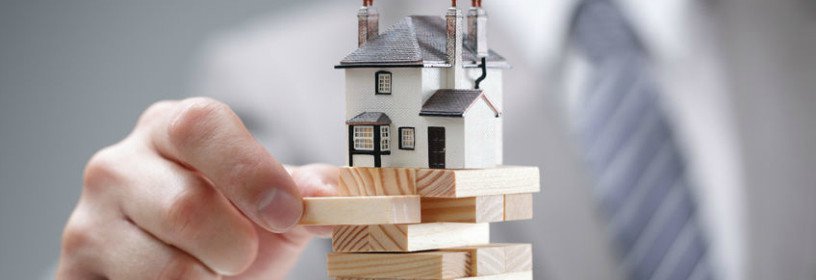 Business man playing jenga with house on top