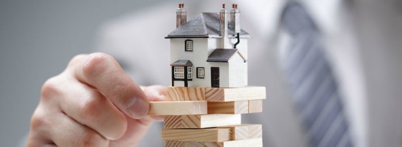 Business man playing jenga with house on top