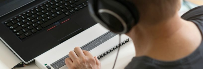 Visually impaired working on computer with braille display and screen reader.
