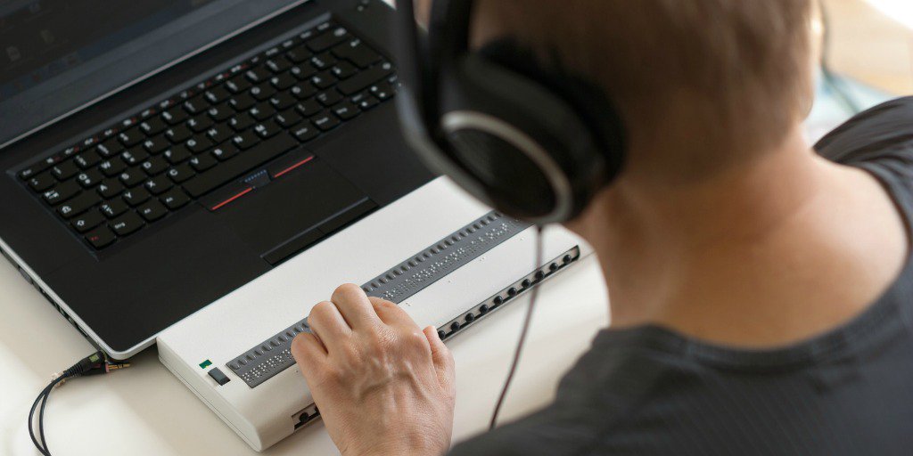 Visually impaired working on computer with braille display and screen reader.