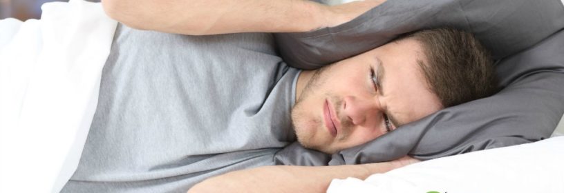 man in bed covering ears with pillow