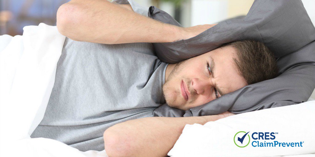 man in bed covering ears with pillow