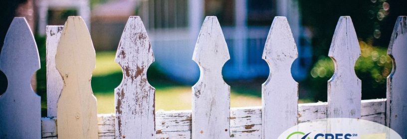 looking through white picket fence toward neighbors house