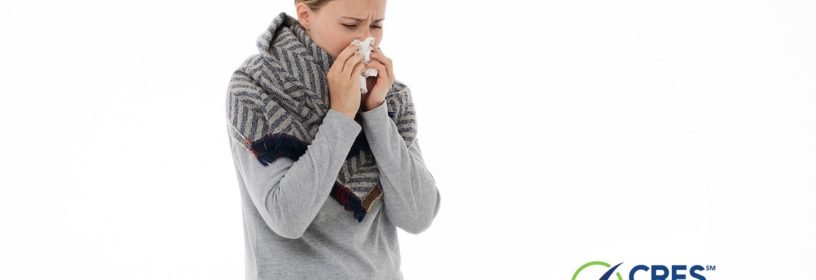 woman with gray sweater and scarf on sneezing into a tissue
