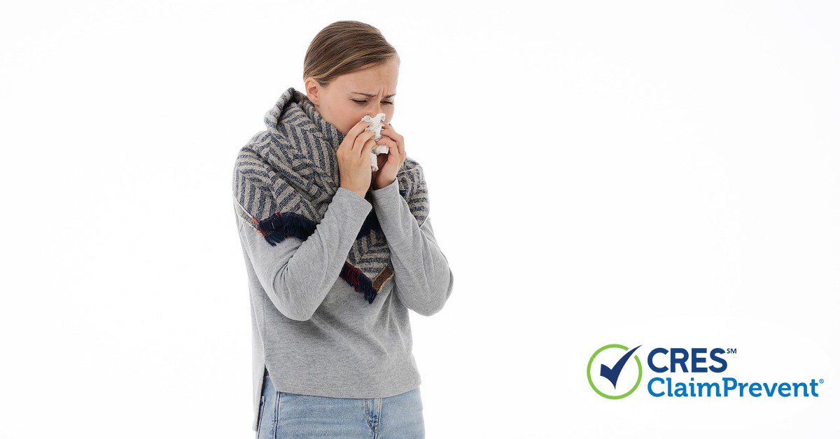 woman with gray sweater and scarf on sneezing into a tissue