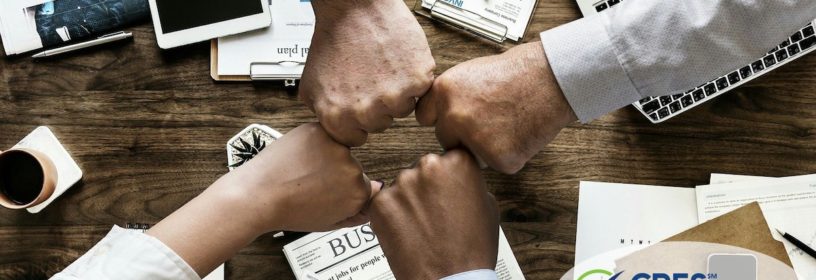 team members putting closed fists together over desk with business items