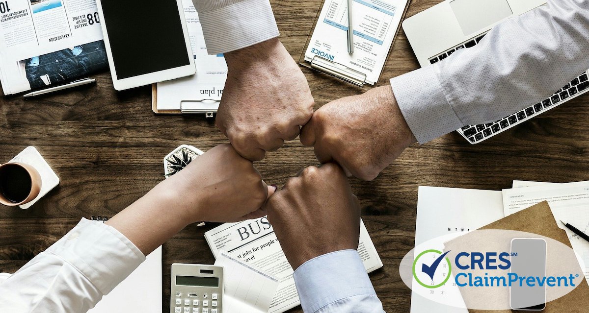 team members putting closed fists together over desk with business items